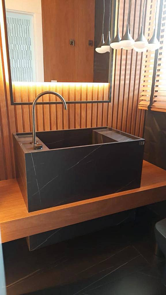 Lavabo em porcelanato escuro com cuba esculpida, iluminação linear e espelho retroiluminado.